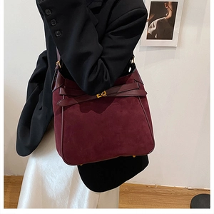 Detail of burgundy faux suede bucket bag with leather straps and metal buckle on model