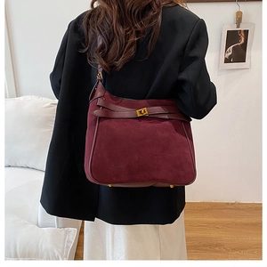 Macro view of burgundy suede bucket bag showing golden twist lock and leather strap detail