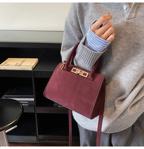 Detail of burgundy suede leather handbag with golden clasp being held by a model