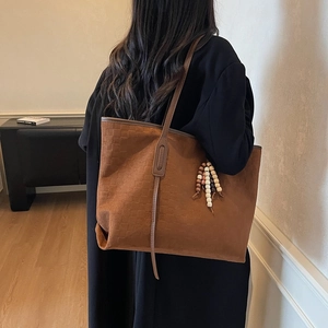Brown suede tote bag with checkered texture and beaded tassel charm carried by model