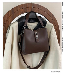 Close-up of dark brown lychee grain leather handbag with metallic lock and wide strap