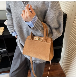 Detail of a brown suede handbag with a gold metal clasp and adjustable shoulder strap