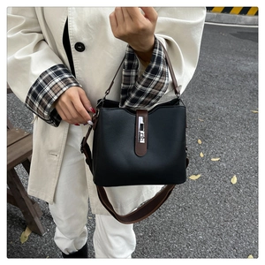 Detail of black textured bucket bag with brown strap styled with a beige trench coat