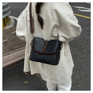 Street view of a black leather bucket bag with brown straps and vintage metal lock closure