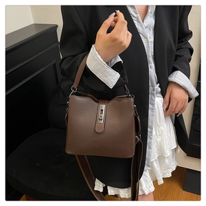 Fashionable dark brown bucket bag held by a model in a black blazer and white dress