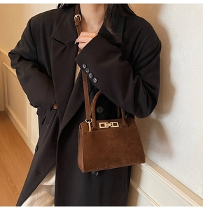 Détail du sac à main marron mat en daim avec boucle dorée porté sur un blazer noir