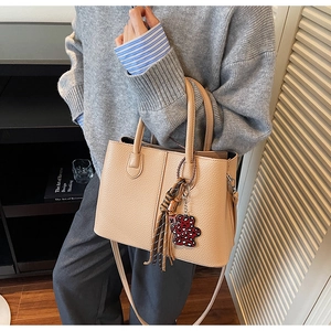 Detail of beige lychee leather handbag with heart bear charm and elegant tassel decor
