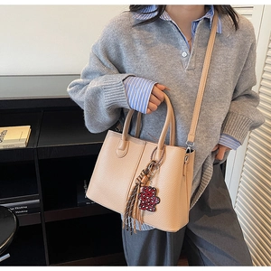 Detail of beige lychee textured handbag with detachable strap and bear pendant