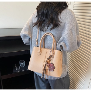 Detail of lychee pattern leather bag with woven tassel and cute bear charm accent