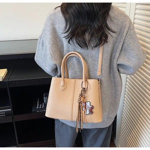 Close-up of light brown lychee grain leather tote bag with tassels and shoulder strap