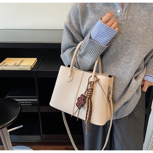 Close-up of beige lychee textured handbag with floral bear and tassel charm details