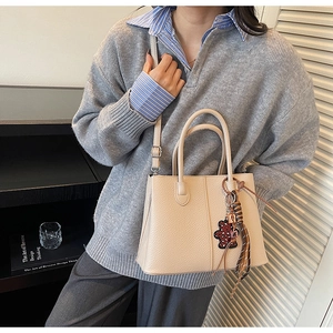 Detail view of beige leather bucket bag with leopard bear charm and braided tassel