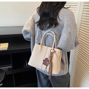 Detailed shot of beige lychee-patterned bucket bag with bear charm and silk scarf adornment