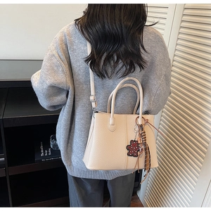 Detailed back view of a beige pebble leather tote bag with a leopard bear charm