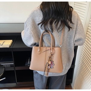 Brown litchi leather bucket bag detail with tassel charm and bear pendant on shoulder strap