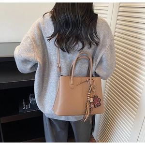 Detail of khaki brown tote bag with leather texture, tassel, and bear charm