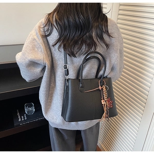 Detail of black pebbled leather tote bag with bear charm and adjustable strap on a model