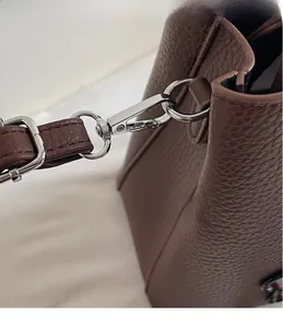 Detail of silver metal hook hardware and litchi grain leather strap on a brown tote bag