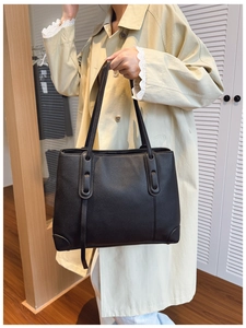 Dettaglio della borsa tote in pelle nera a grana indossata da una modella in casa