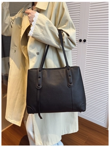 Borsa tote nera in pelle martellata indossata a spalla da una modella in trench chic