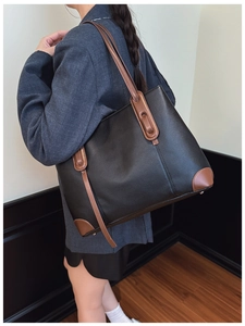 Vista laterale di una borsa tote in pelle nera con finiture marroni su una modella