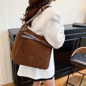 Brown faux suede bucket bag with gold metal buckle shown on a model in a white blazer