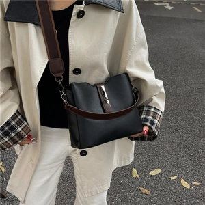 Chic black leather bucket bag with brown straps and silver lock shown in a street setting