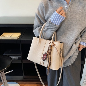 Minimalist beige pebble leather bucket bag shown as a crossbody on model in urban setting