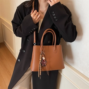 Brown lychee leather bucket handbag with adjustable strap and decorative charm