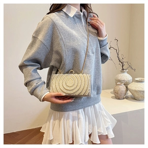 Dettaglio di pochette da sera con perle bianche, cristalli e tracolla a catena d'oro
