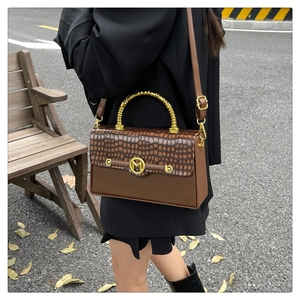 Street style shot of brown croc-pattern leather handbag with golden spiral handle