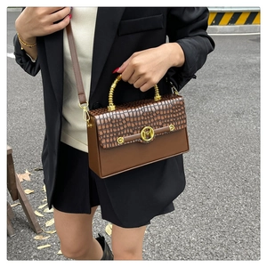 Detail of a brown leather box bag with crocodile texture and spiral gold handle