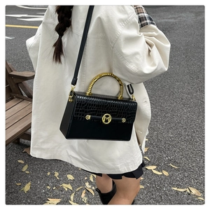 Detail of black PU box bag with crocodile pattern and golden M logo and spiral ring handle