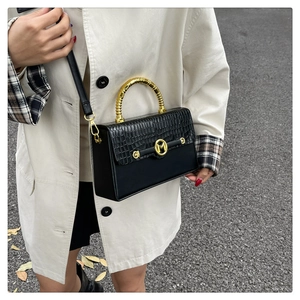 Detail of black faux crocodile skin handbag with golden spiral handle and M logo emblem