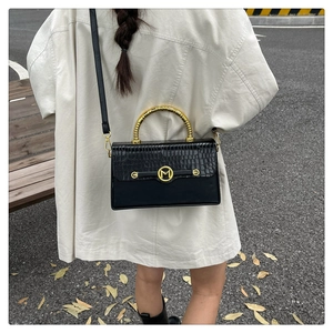 Outdoor view of a black PU leather box bag with gold bamboo handle and embossed texture