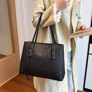 Borsa tote classica in pelle nera martellata indossata da modella in cappotto beige