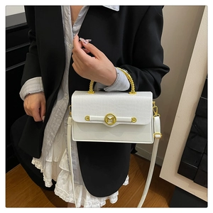 Detail of white crocodile embossed box bag with gold handle and M logo on black blazer