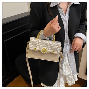 Detail of light beige box bag featuring crocodile texture and gold M-shaped metal buckle