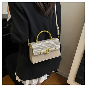 Detail of beige faux crocodile leather bag with gold M-buckle and circular metal handle