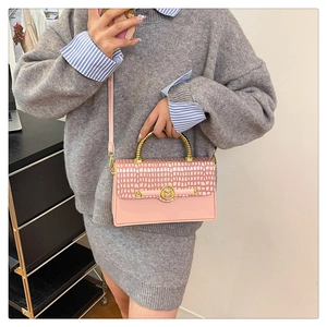 Detail of pink crossbody bag with crocodile texture and golden spiral handle
