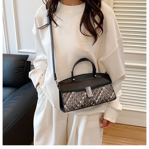 Detail of woven texture handbag featuring a black leather flap and metallic lock