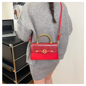 Detail of red croc-embossed handbag with bamboo handle and gold M-logo on a side profile
