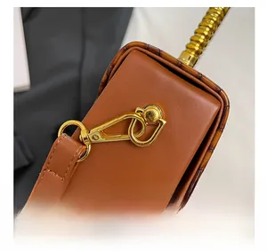 Detail of golden metal swivel hook and bamboo-textured trim on brown leather bag