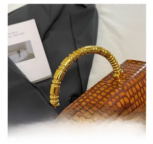 Detailed macro view of the golden bamboo handle and brown croc-embossed leather bag