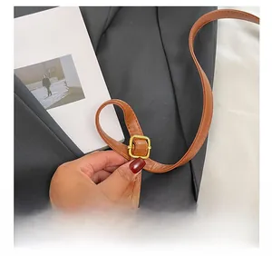 Detail of brown leather shoulder strap featuring an adjustable gold-tone metal buckle
