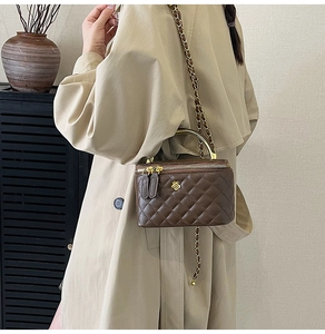 Sac boîte matelassé marron avec poignée métal et bandoulière porté sur un trench-coat