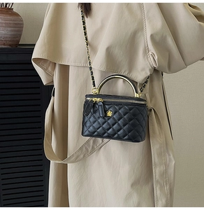 Détail du sac boîte noir matelassé avec poignée dorée et fermoir fleur métallique