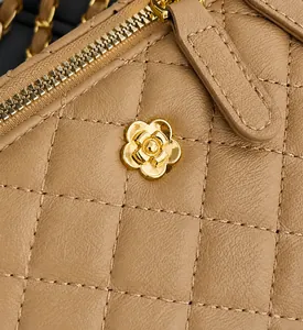 Détail du sac en cuir beige matelassé avec fleur de camélia dorée et surpiqûres précises