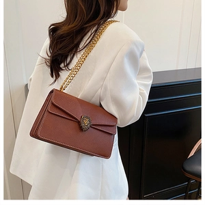 Detail view of brown pebbled leather shoulder bag with gold lion head clasp and chain