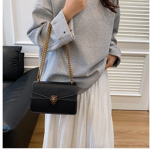 Detail of black crossbody bag with white stitching, gold lion head clasp and chain strap